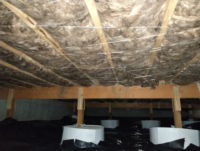 Crawlspace with batt insulation between floor joists and black vapor barrier below