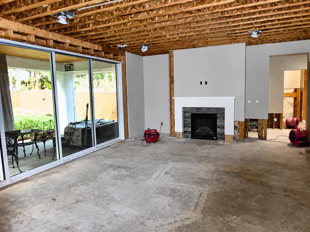 Great room stripped to the subfloor with exposed TGI joists overhead and air movers drying