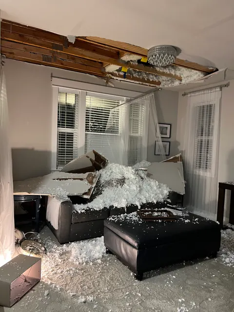 Partially collapsed living room ceiling with insulation and drywall piled on the sofa and ottoman