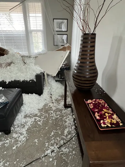 Wet blown-in insulation spread across the living room floor beside a console table